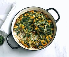 a pan filled with spinach and cheese on top of a white tablecloth next to two small bowls