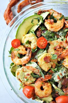 shrimp salad with avocado and tomatoes in a glass bowl on a white table