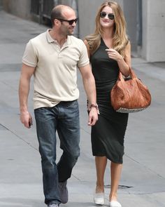 a man and woman are walking down the street holding hands, one is carrying a purse