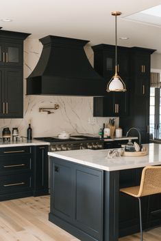 a kitchen with black cabinets and white marble counter tops, an island in the middle