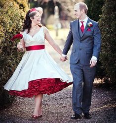 a man and woman dressed in formal wear holding hands while walking down a path between bushes