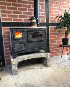 an old fashioned stove sitting in front of a brick wall next to a potted plant