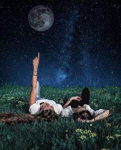 two people are laying in the grass with their hands up to the stars above them