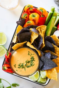 a tray filled with tortilla chips and dip surrounded by fresh veggies