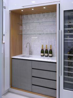 two bottles of wine sitting on top of a counter next to a glass case filled with glasses