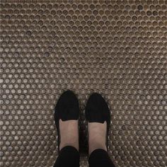 a person wearing black shoes standing in front of a metal grate with circles on it