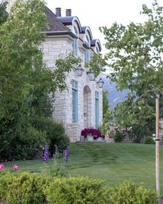 a large house sitting in the middle of a lush green field next to trees and bushes