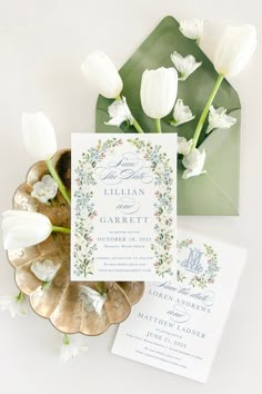 the wedding stationery is set on top of a gold plate with white tulips