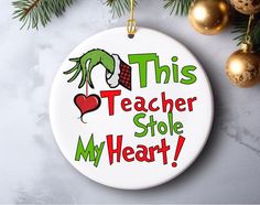 this teacher stole my heart christmas ornament on a white background with gold ornaments