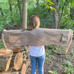 a woman carrying a large knitted blanket over her shoulders in the woods with logs