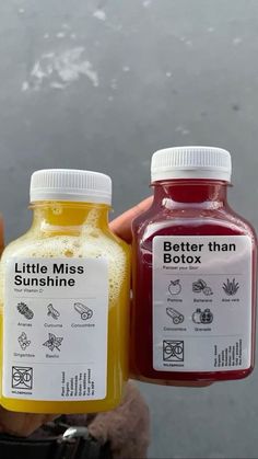 two bottles of juice sitting next to each other in front of a person's hand