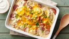 a casserole dish with ham, cheese and sour cream on top next to a spoon