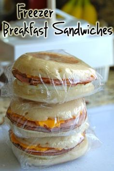 three sandwiches wrapped in plastic sitting on top of a white counter with text overlay that reads freezer breakfast sandwiches