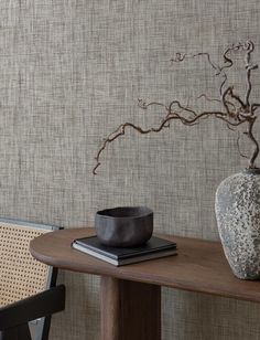 a vase sitting on top of a wooden table next to a wall with a plant in it