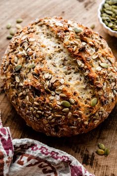 a loaf of bread sitting on top of a wooden table next to two bowls filled with seeds