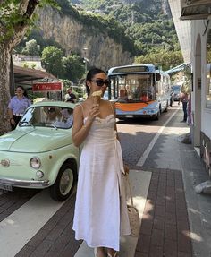 a woman in a white dress eating an ice cream cone on the side of the road