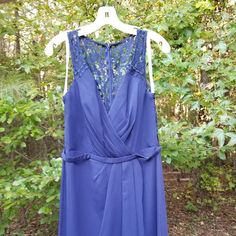 a blue dress hanging on a white hanger in front of some green trees and bushes