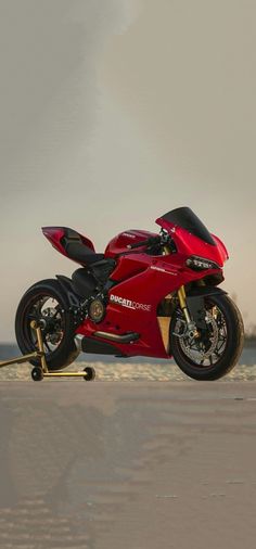 a red motorcycle parked on top of a sandy beach