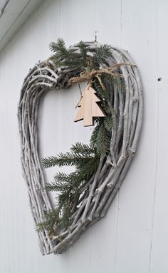 a heart shaped wreath hanging on the side of a white building with pine cones and evergreen branches