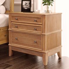 a wooden dresser sitting on top of a hard wood floor next to a white bed