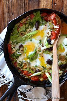 a skillet filled with eggs and vegetables on top of a wooden table next to utensils