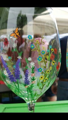 two hand painted wine glasses sitting on top of a green table next to each other