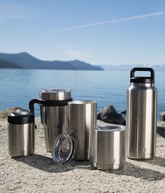 thermos and cups are sitting on the sand by the water