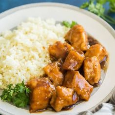 a white plate topped with rice and chicken next to broccoli on a blue table