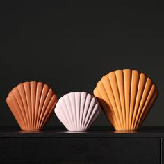 three seashells sitting on top of a wooden table in front of a black wall