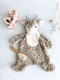 a stuffed animal laying on top of a white blanket next to baby shoes and a wooden spoon