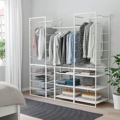 a white closet with clothes hanging on the wall and a bed in the foreground