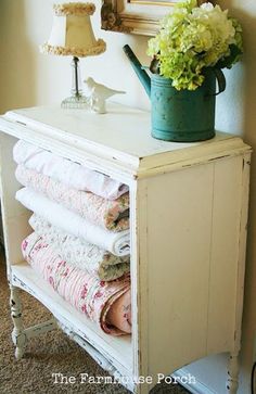 a white cabinet with many folded towels on it and a blue watering can next to it