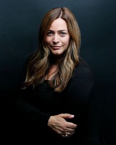 a woman standing with her arms crossed and looking at the camera, in front of a black background