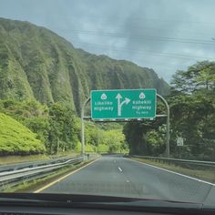 a highway sign on the side of a road with mountains in the backgroud