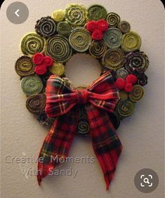 a christmas wreath made out of buttons with a red bow hanging on the wall next to it