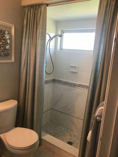 a white toilet sitting next to a shower in a bathroom under a window with curtains