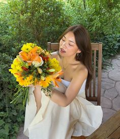 a woman sitting on a bench holding a bouquet of yellow and orange flowers in her hands