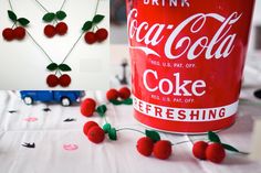 a coca - cola can with cherries attached to it and some other items surrounding it