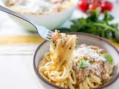 a fork full of pasta with meat sauce and parmesan cheese on top in a bowl