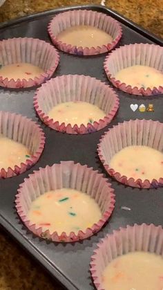 nine cupcakes in pink paper cups sitting on a baking tray with white icing