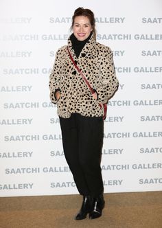 a woman standing in front of a wall wearing a leopard print coat and black pants