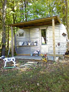 a dog is standing in front of a small metal shed with a stove on the porch