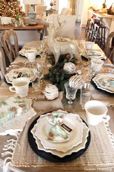 a dining room table set for christmas with plates, cups and saucers on it