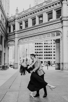 a man and woman dancing on the sidewalk in front of an old building with tall buildings