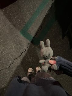 a person holding a stuffed animal in their hand while standing next to someone's feet