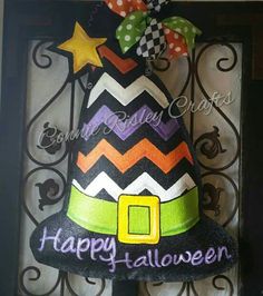 a decorated halloween hat hanging on a wrought iron gate with the words happy halloween written in purple, orange and green