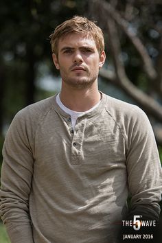 a man in a tan shirt holding a white frisbee and looking at the camera