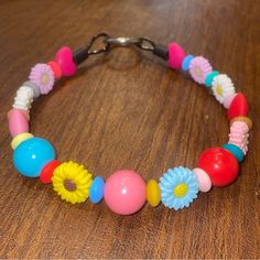 a bracelet made out of plastic beads and flowers on a wooden table with a metal hook