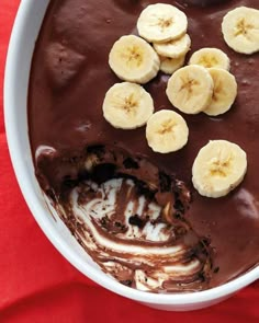 a bowl filled with chocolate and bananas on top of a red table cloth next to a spoon