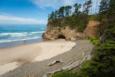 two people are walking on the beach near some trees and water with cliffs in the background